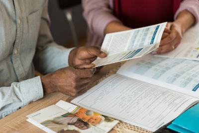 Two people, one holding a health insurance brochure, discuss health coverage companies options during a consultation.