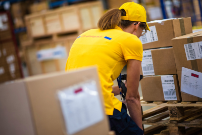 A postal worker in a yellow uniform is sorting packages in a warehouse, highlighting the physical demands of the job which could lead to postal worker disability.