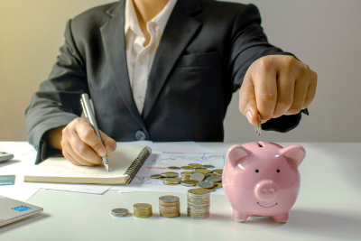 A person adding coins to a piggy bank with stacks of coins, representing savings for TSP contribution limits.